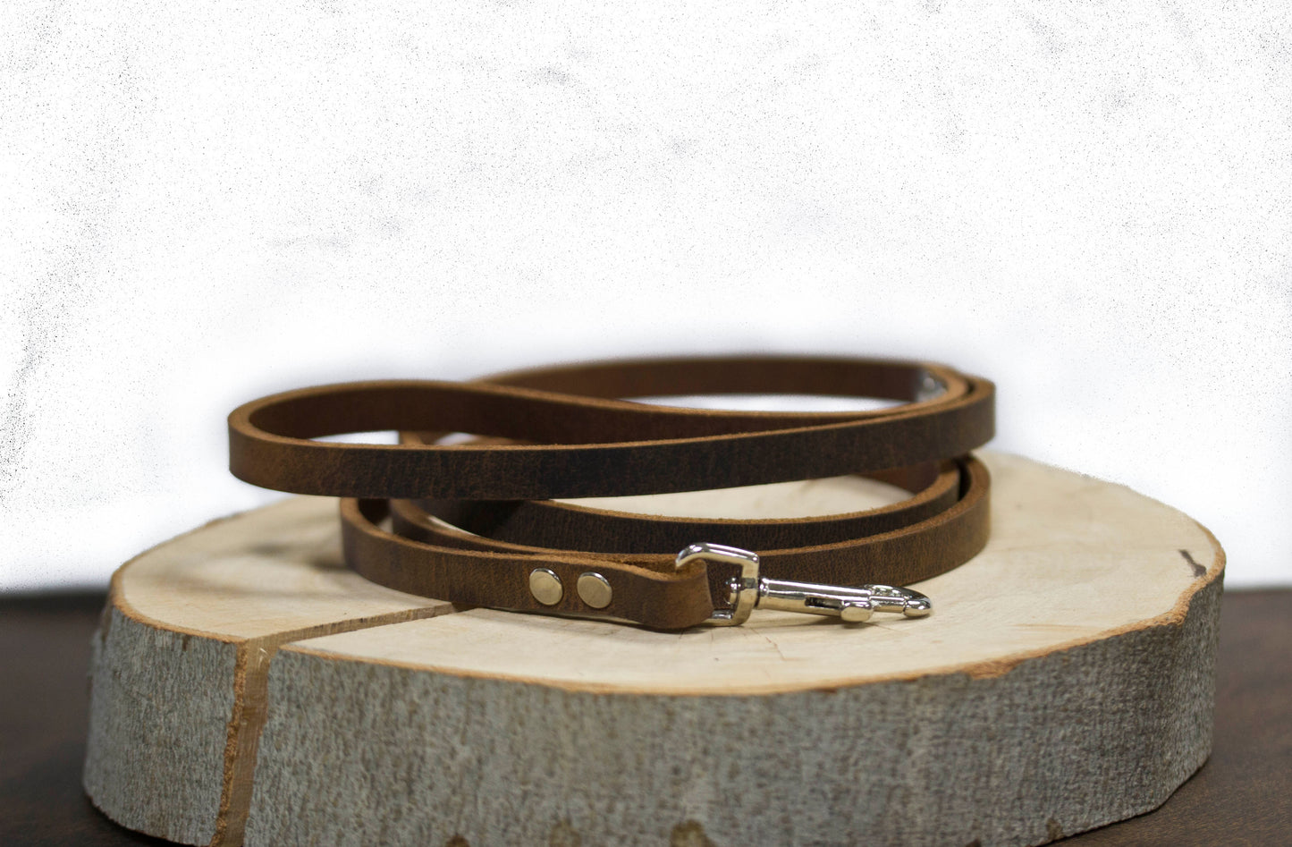 Brown natural leather dog leash coiled on wooden charger - vintage aesthetic handcrafted leash