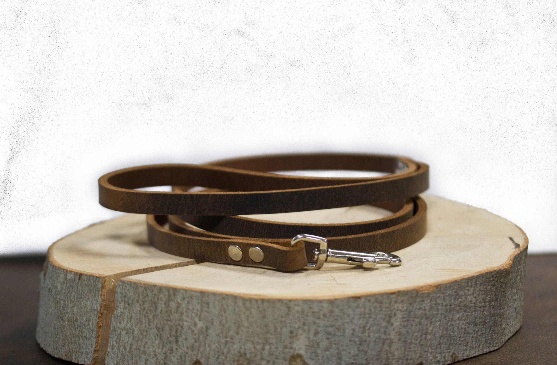 Brown natural leather dog leash coiled on wooden charger - vintage aesthetic handcrafted leash